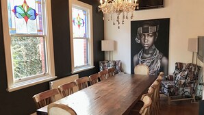 Un comedor con una larga mesa de madera, varias sillas, un candelabro, ventanas de vitral y un retrato grande en la pared.