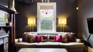 Un salón acogedor con sofá, dos lámparas, chimenea y una ventana con vidrio decorativo.