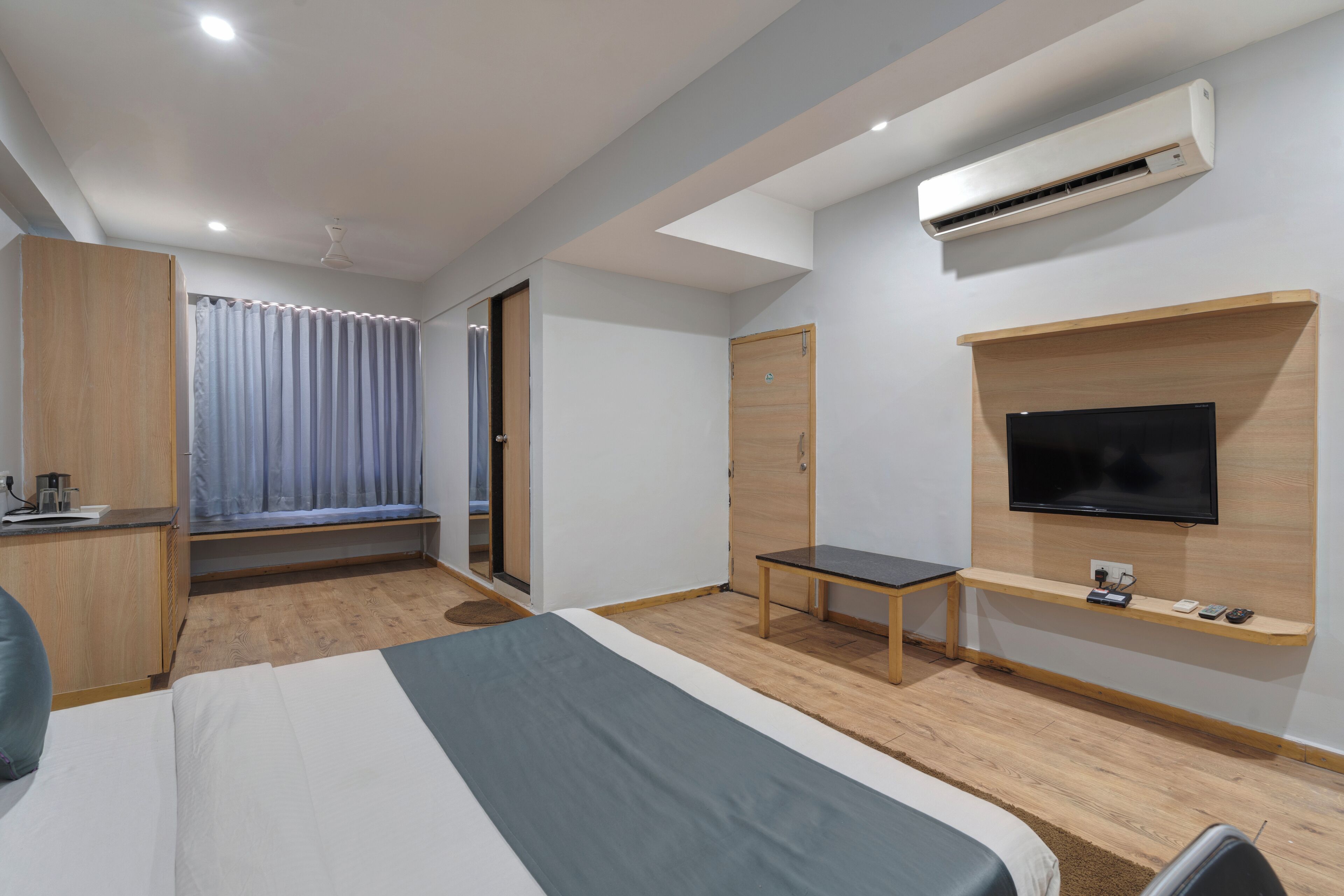 Quarto de hotel moderno com cama, escrivaninha, televisão e ar condicionado.