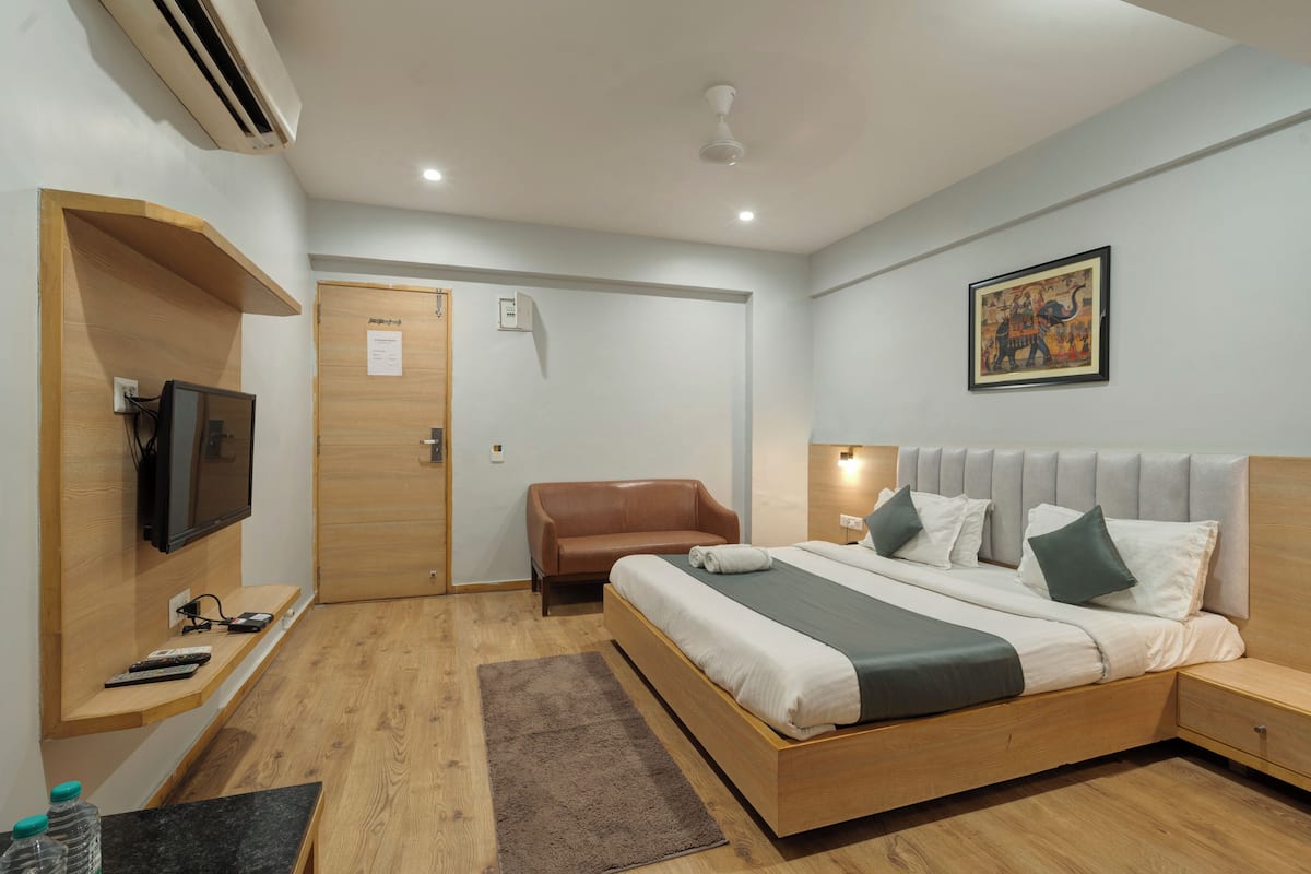 Une chambre d’hôtel moderne avec un lit en bois, une télévision, un canapé et un tableau au mur.