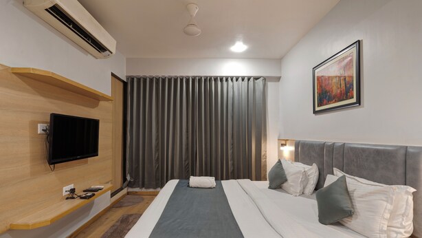 Una habitación de hotel moderna con una cama grande, un televisor de pantalla plana, un equipo de aire acondicionado y un cuadro en la pared.