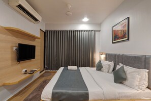 A modern hotel room with a large bed, a flat-screen TV, an air conditioning unit, and a painting on the wall. - Hotel Berlin (Gandhinagar)