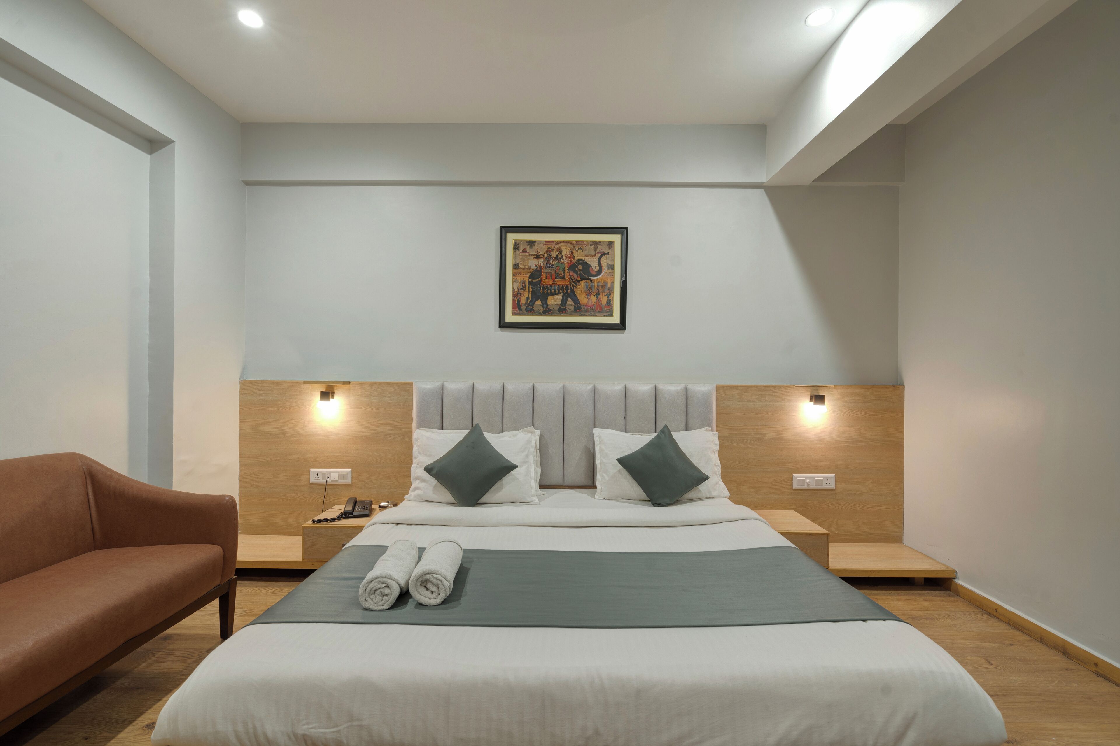 A modern hotel room with a large bed, two bedside tables, a brown sofa, and a painting on the wall.