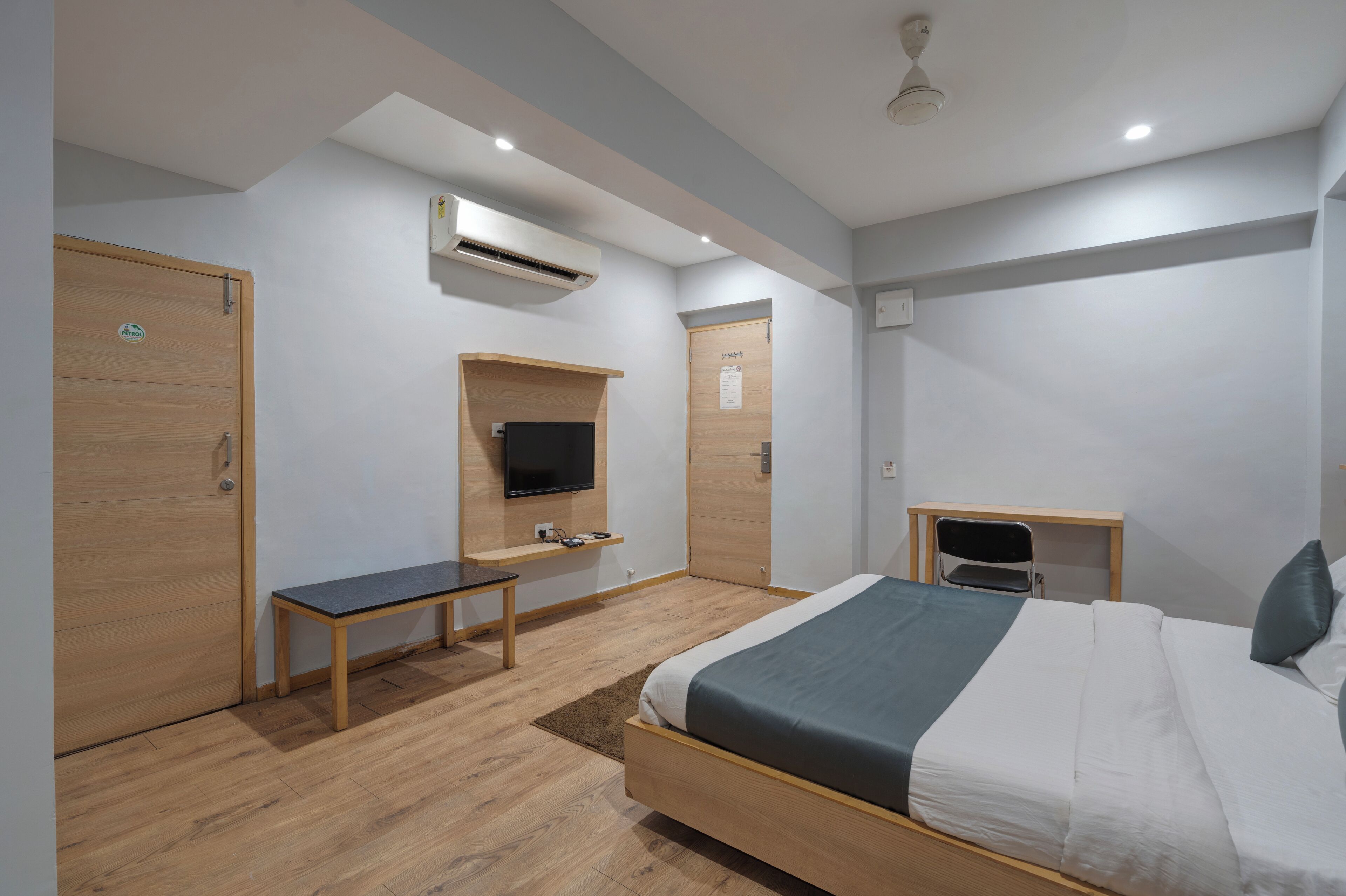 A modern hotel room with a wooden bed, a desk, a television, and a wardrobe.