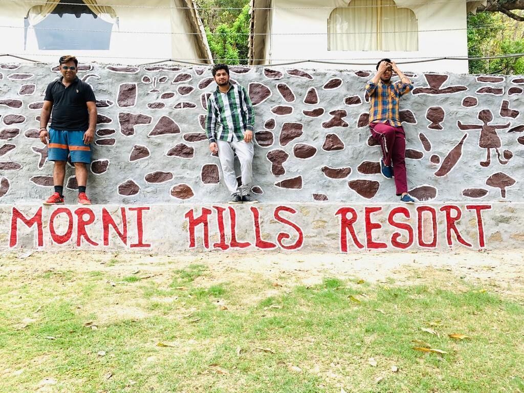 Three people standing in front of a wall with the text "MORNI MILLS RESORT" painted on it.