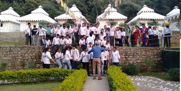 A group of people gathered in an outdoor setting with traditional white-roofed buildings in the background. - Morni Hills Resort (Panchkula)