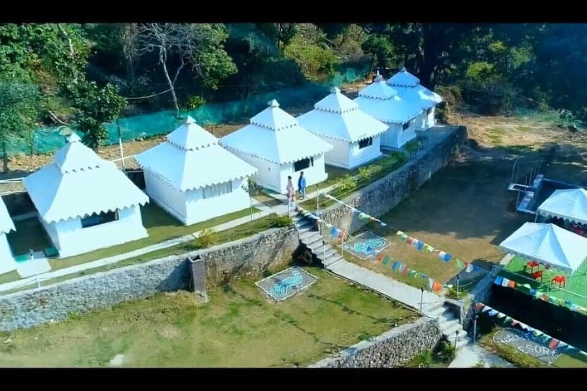 A series of white tents with conical roofs, arranged in a row along a stone wall, adjacent to a swimming pool area.
