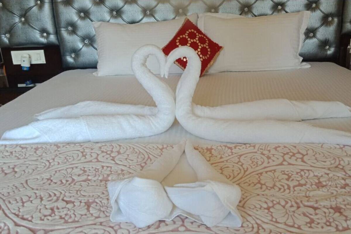 A bed with a tufted headboard, a red decorative pillow, and a swan-shaped towel arrangement.