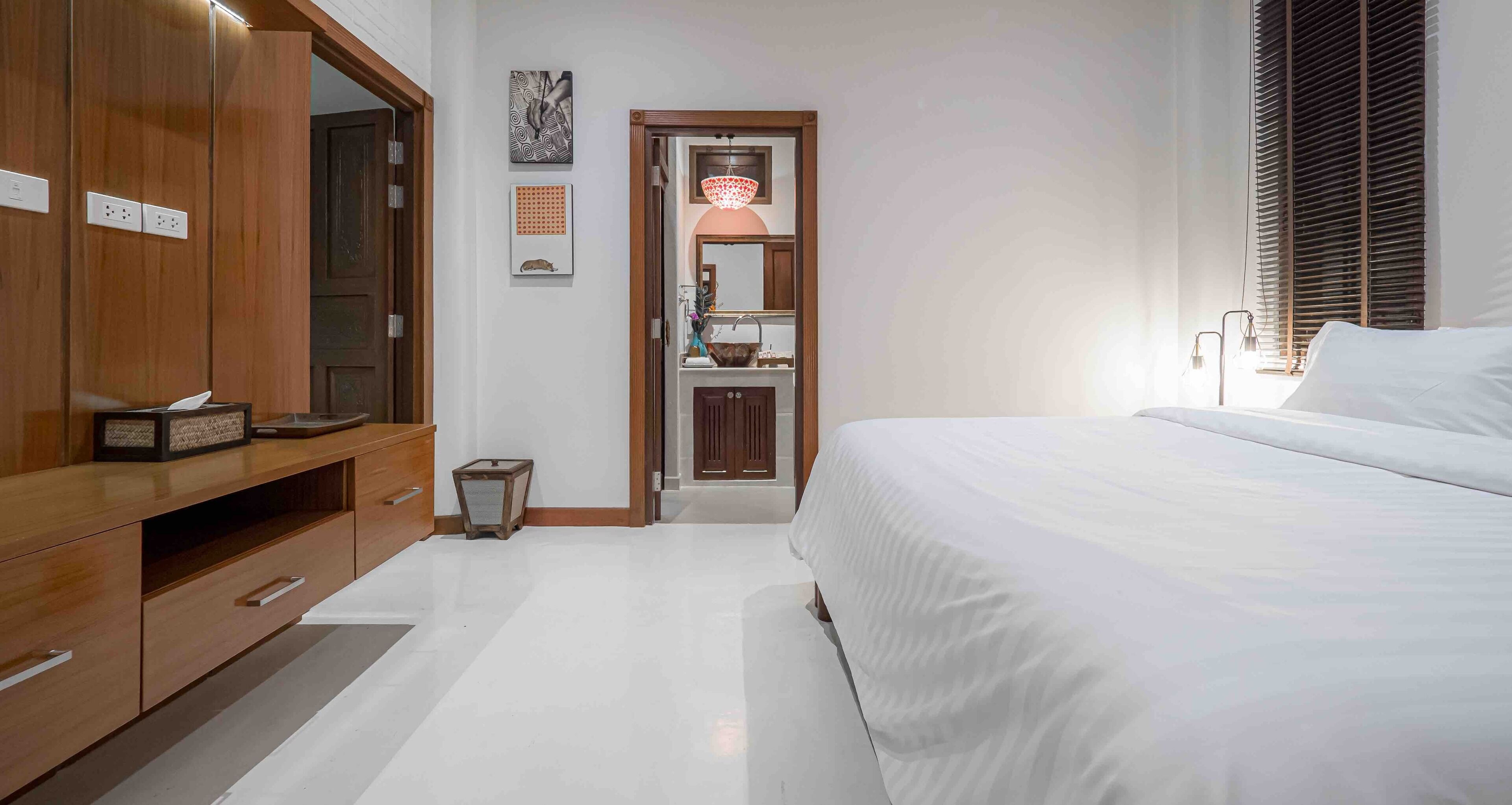 A bedroom with a large bed, wooden wardrobe, and a small bathroom with a mirror and sink.
