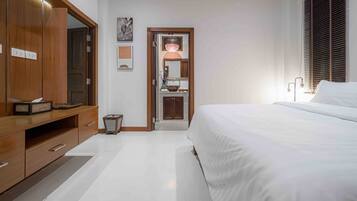 A bedroom with a large bed, wooden wardrobe, and a small bathroom with a mirror and sink.