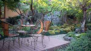 A wooden deck with metal chairs and a table, surrounded by greenery and rocks. - Chiang Mai's Best Garden Paradise Villa, A/C, Free Breakfast, Pool, Rental Van (Nam Phrae)
