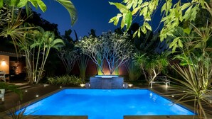 A swimming pool with a waterfall feature, surrounded by tropical plants and a stone bench. - Chiang Mai's Best Garden Paradise Villa, A/C, Free Breakfast, Pool, Rental Van (Nam Phrae)