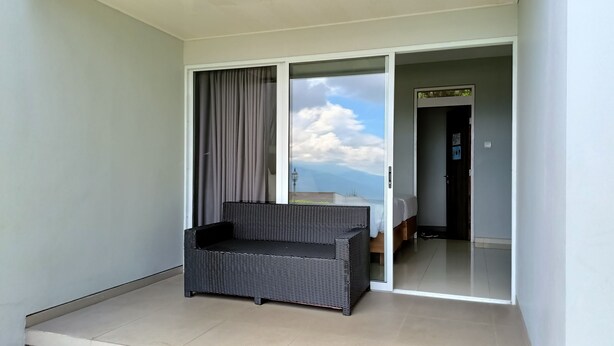 A balcony with a wicker chair, a bed, and a view of the sky. - Amanda Hills Bandungan (Bandungan)