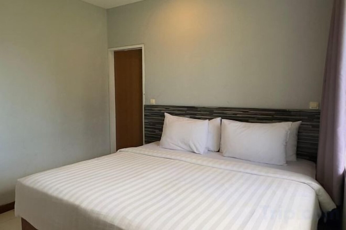 A bed with a headboard, a door, and a light fixture on the wall.
