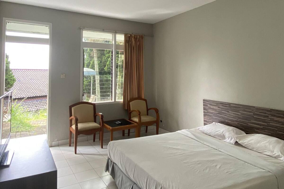 Une chambre d’hôtel avec un lit, deux chaises, un bureau et une fenêtre avec des rideaux.
