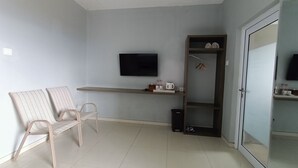 A small, modern room with a flat-screen TV mounted on the wall, a wooden shelf with a kettle and bottles, a pair of chairs, and a door leading to another room. - Amanda Hills Bandungan (Bandungan)