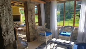 A rustic room with stone walls, wicker furniture, and large windows offering a view of a green landscape. - Affi Lande Boetiek Guest Farm (Fouriesburg)