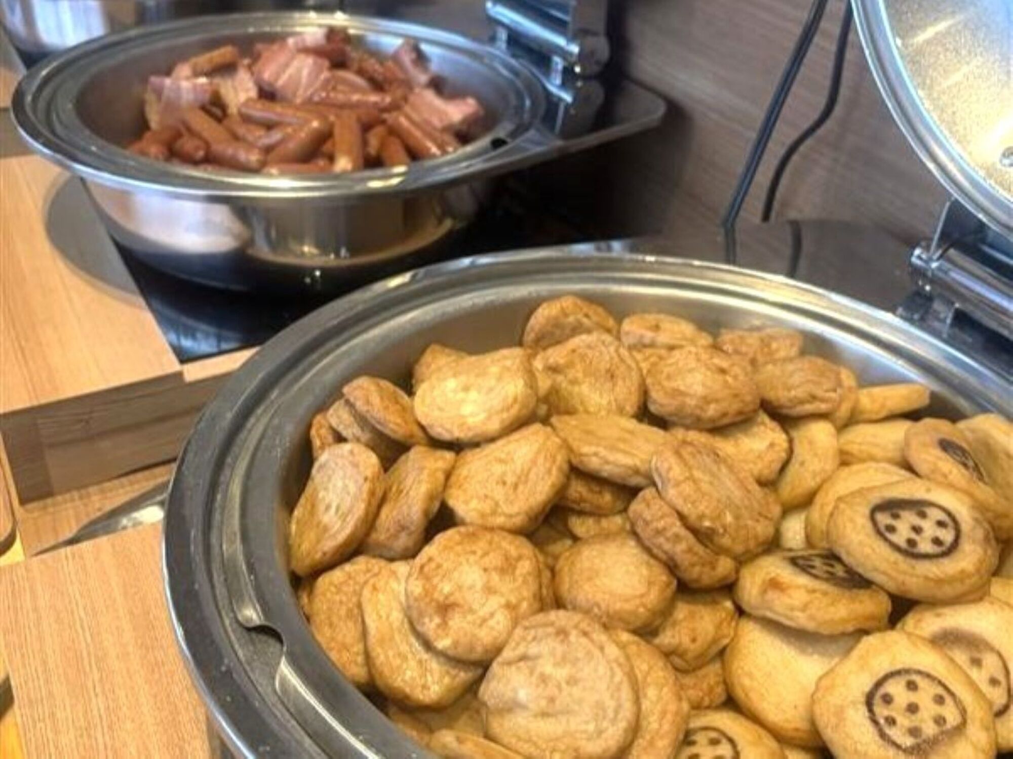 A buffet table with a variety of food items including sliced sausages and round, flat pastries.