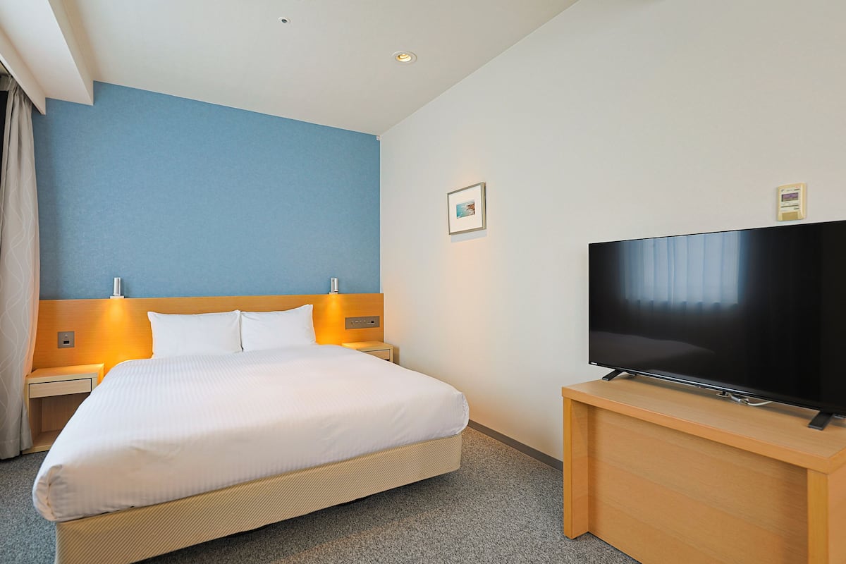 Une chambre d’hôtel avec un lit, un téléviseur posé sur un meuble en bois et une table de chevet avec une lampe.
