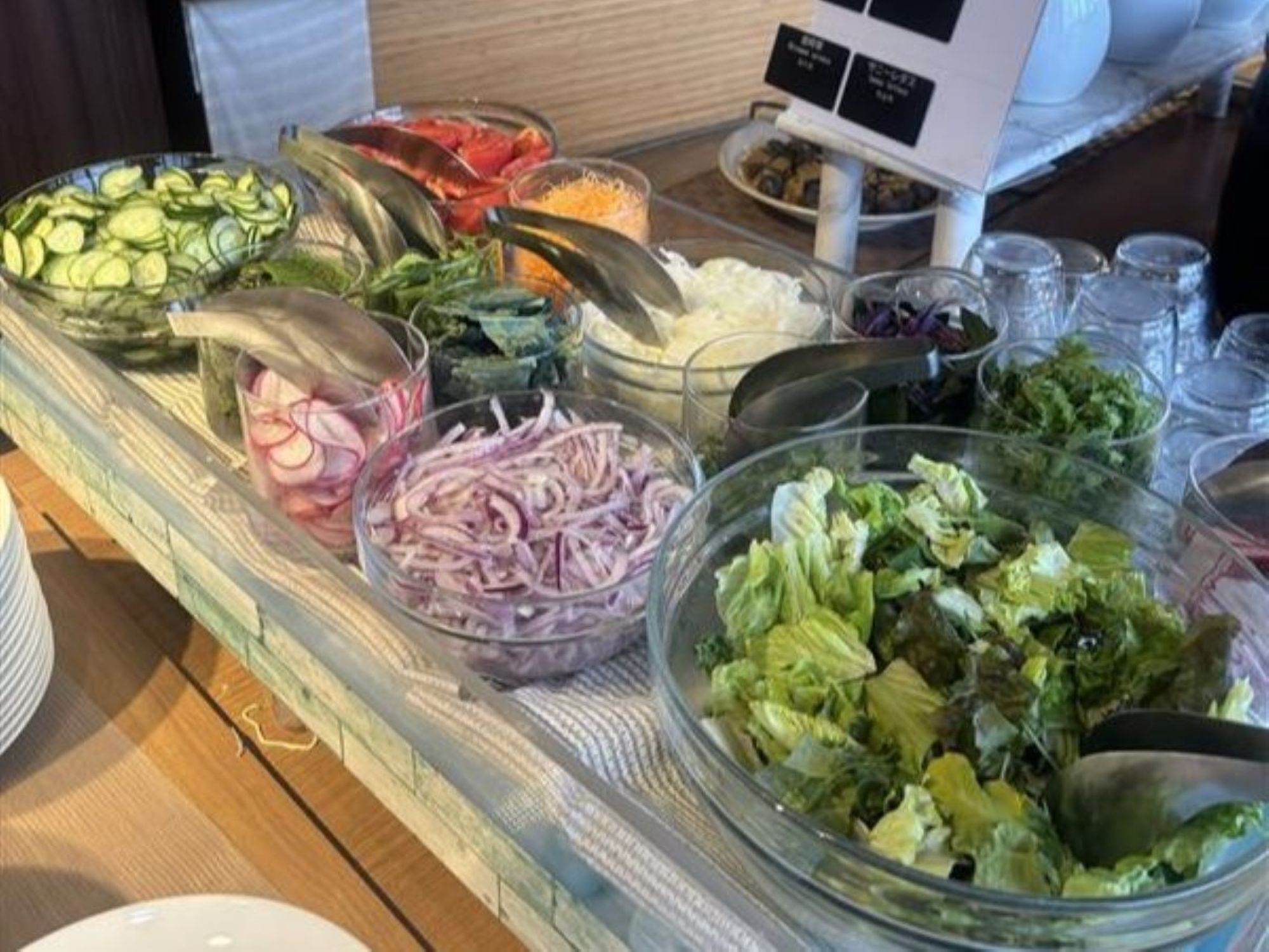 A buffet with various food items including sliced cucumbers, tomatoes, onions, and lettuce.