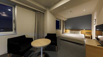 Habitación de hotel con cama, escritorio, silla, mesa redonda y vista de la ciudad de noche.