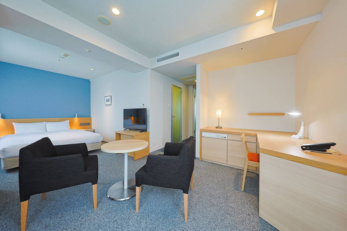 Une chambre d’hôtel comprenant un lit, deux chaises, un bureau, une télévision et une petite table.