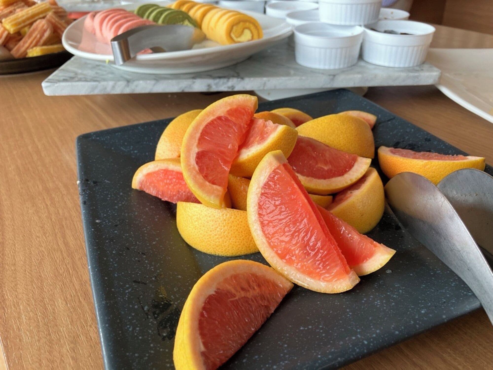 A black cutting board with sliced grapefruits and a knife on a wooden table.