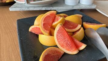 A black cutting board with sliced grapefruits and a knife on a wooden table.