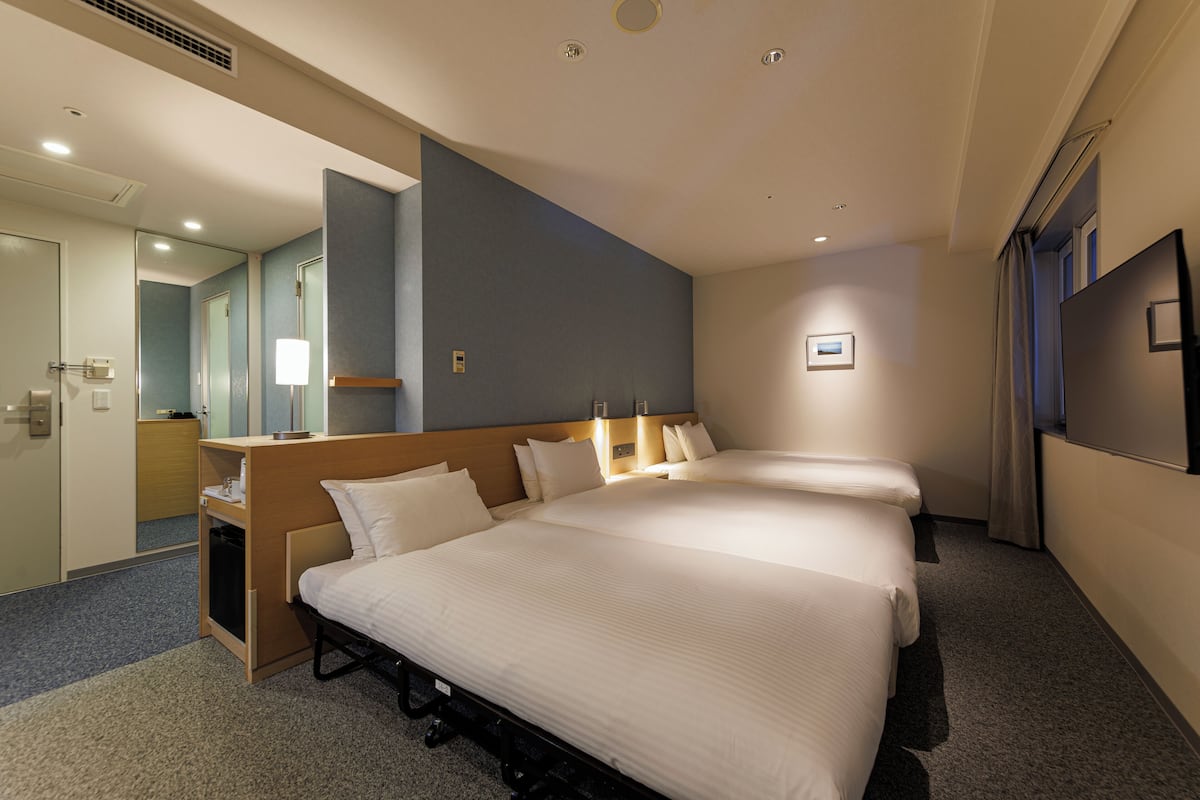 Une chambre d’hôtel avec deux lits, un bureau, un miroir et une télévision.