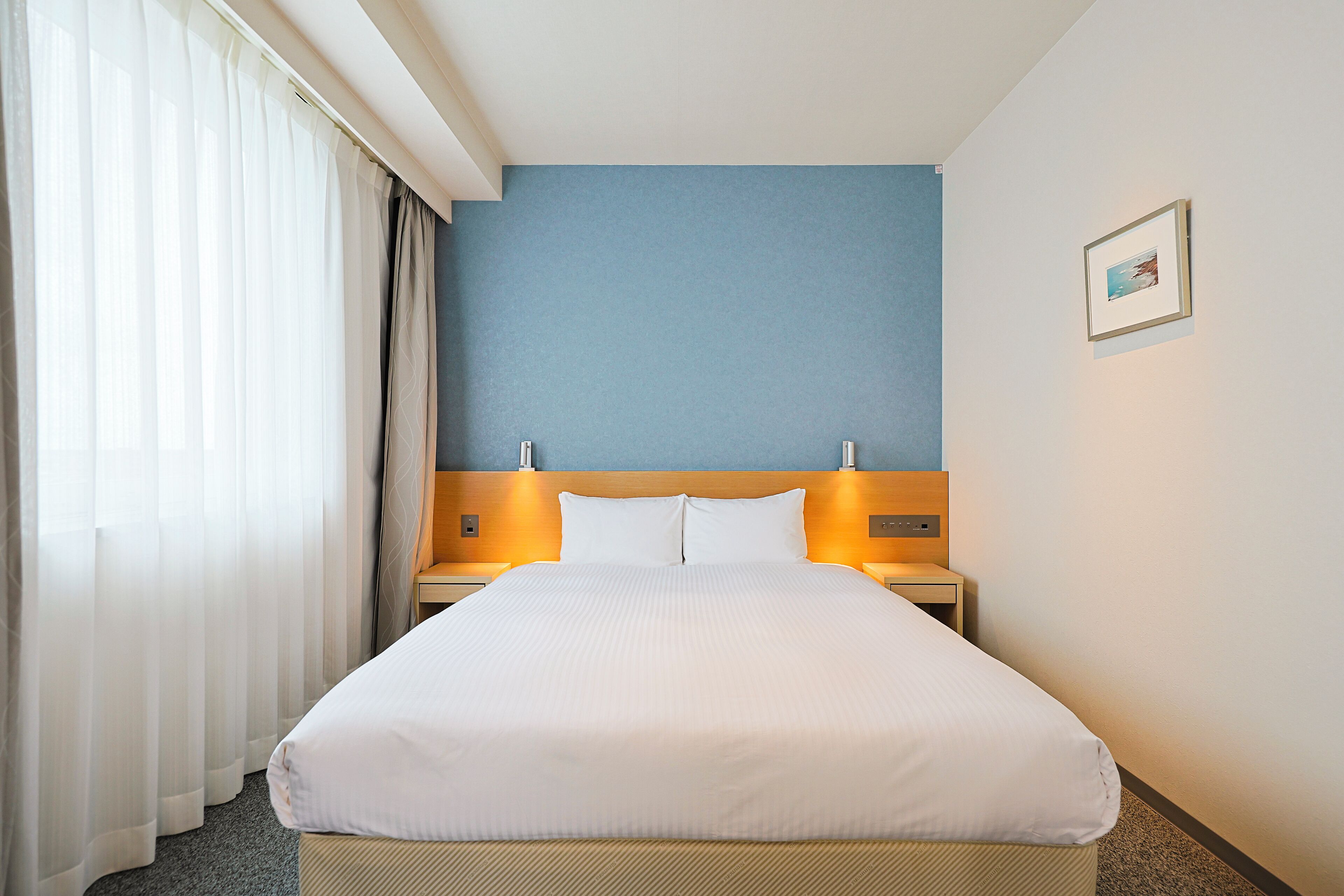 A hotel room with a large bed, a headboard, two bedside tables, and a picture on the wall.