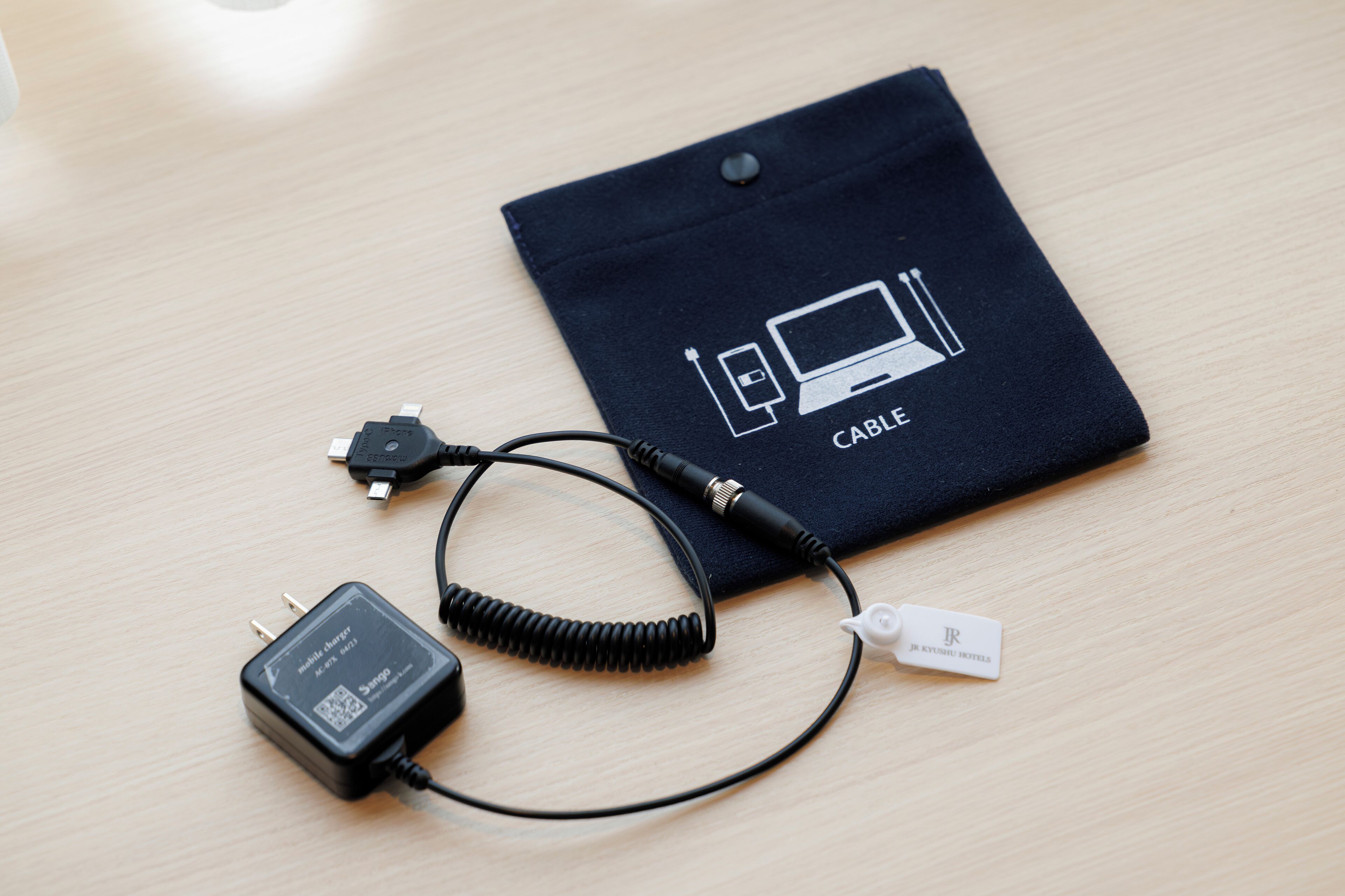 Een zwarte kabelpouch met een kabel en een stroomadapter op een houten ondergrond.