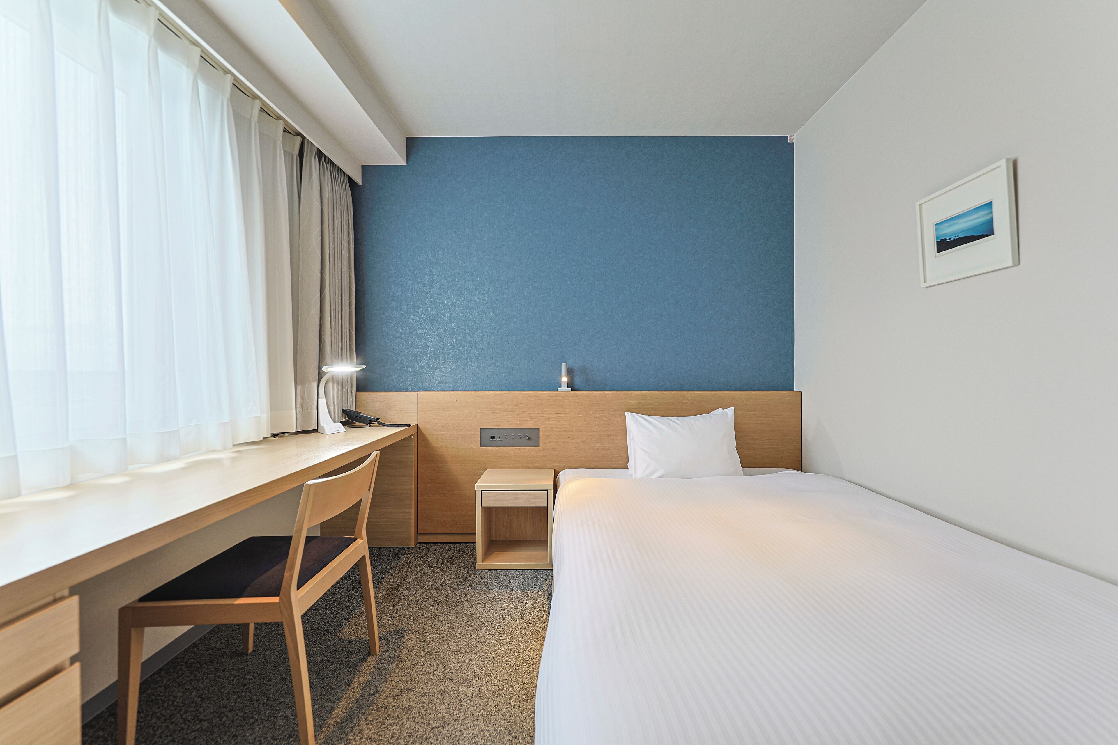 A hotel room with a bed, a desk, a chair, and a nightstand.