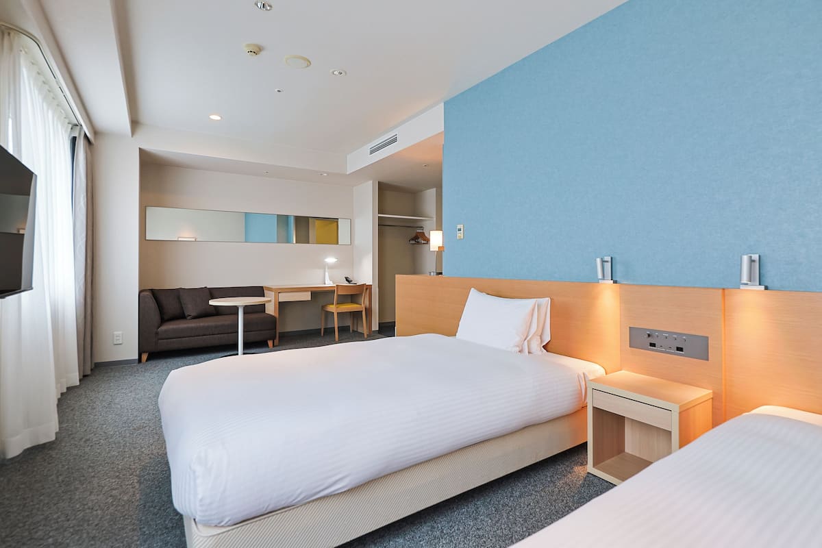 Une chambre d’hôtel avec deux lits, un bureau, une chaise, un canapé et un grand miroir.