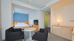 A hotel room with a bed, a TV, a small table, two chairs, a desk with a lamp, and a green door. - JR KYUSHU HOTEL Miyazaki (Miyazaki)