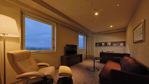 A modern hotel room with a large window, a flat-screen TV, a sofa, a chair, and a small table. - JR KYUSHU HOTEL Miyazaki (Miyazaki)