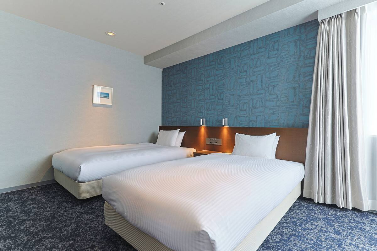 Une chambre d’hôtel avec deux lits, un mur orné d’un motif bleu et une grande fenêtre avec des rideaux.