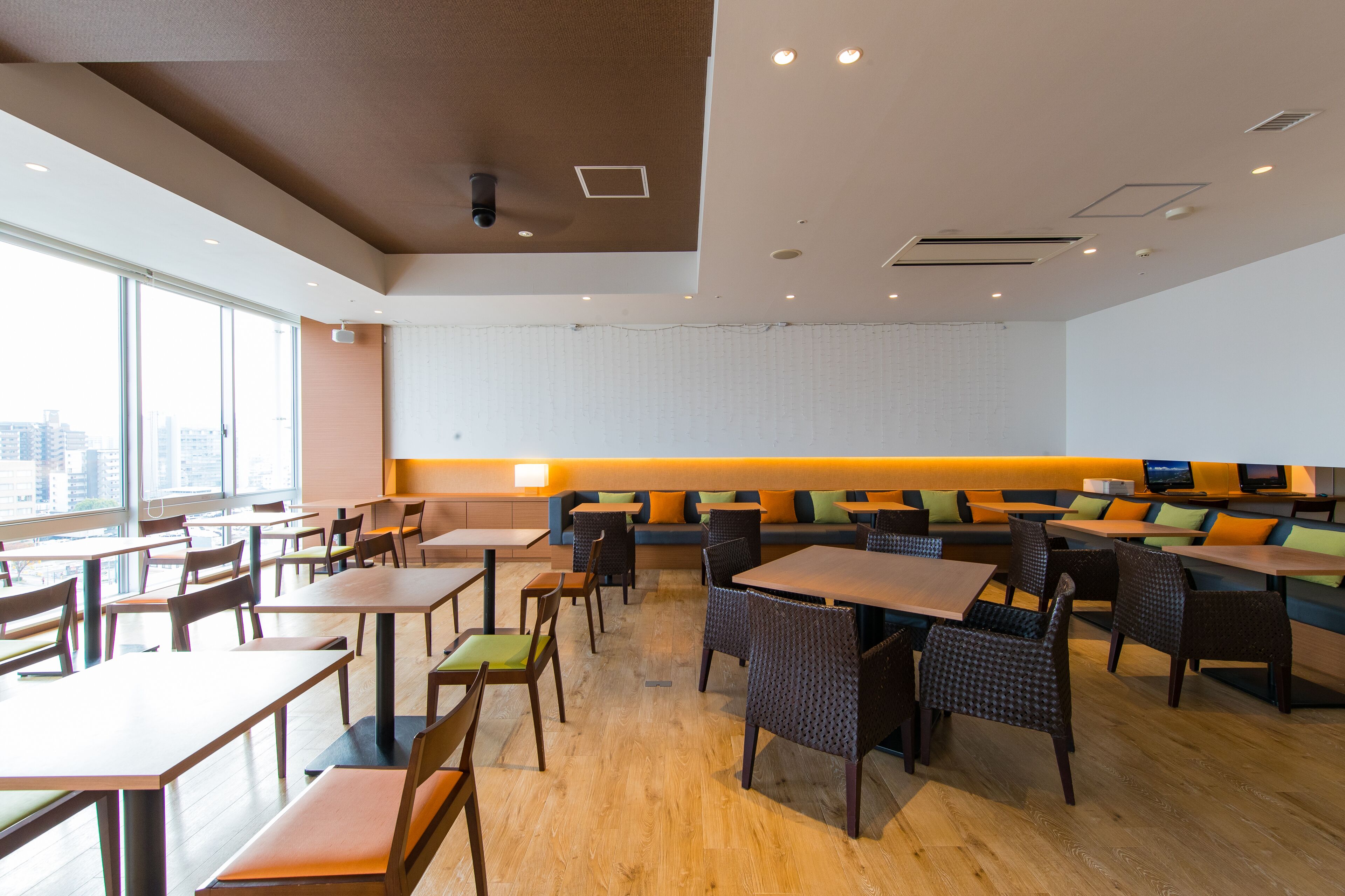 A spacious dining area with high tables and chairs, a long counter, and a seating area with cushions.
