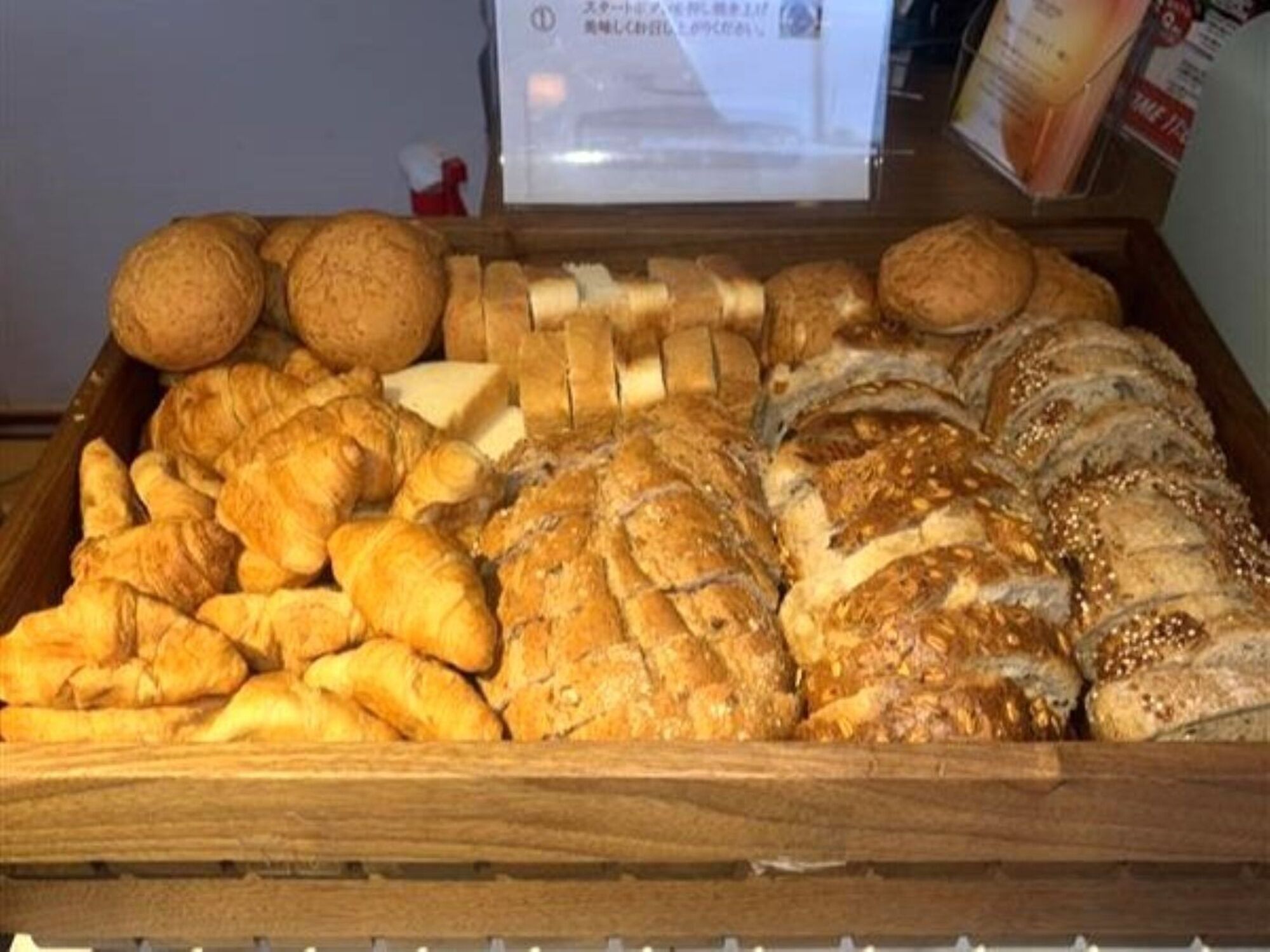 Una bandeja de madera llena de diferentes tipos de pan, incluyendo croissants y pan en rebanadas.