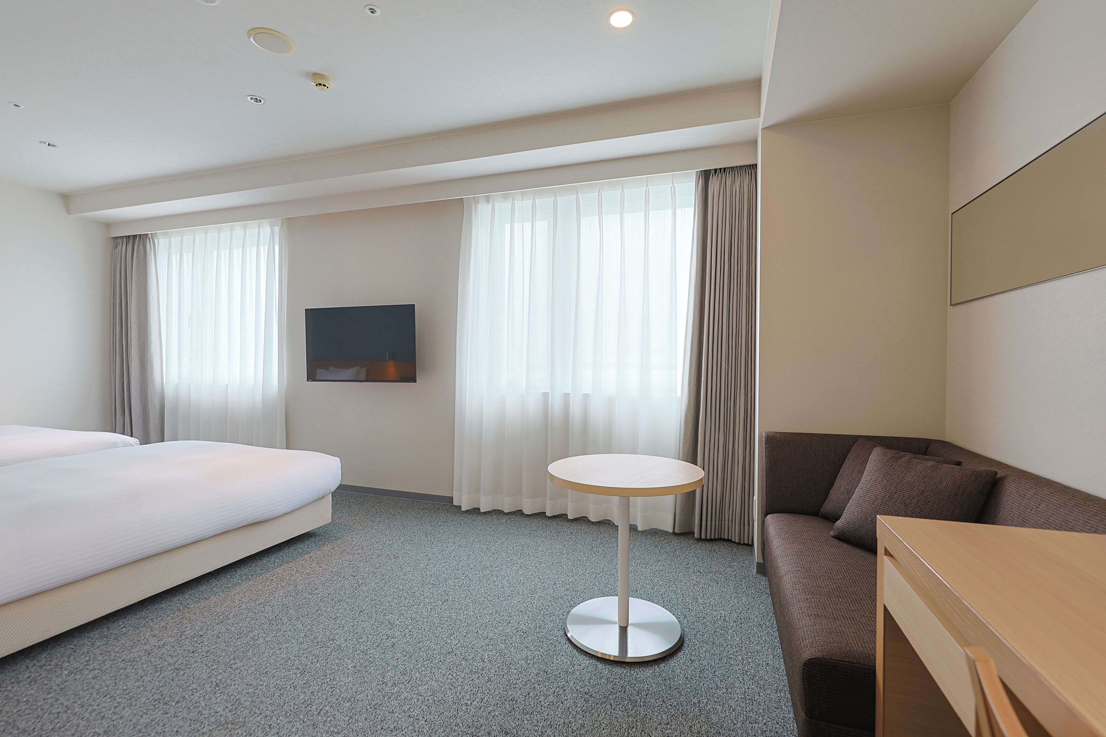 Una habitación de hotel con cama, una mesa redonda, sofá y televisor en la pared.