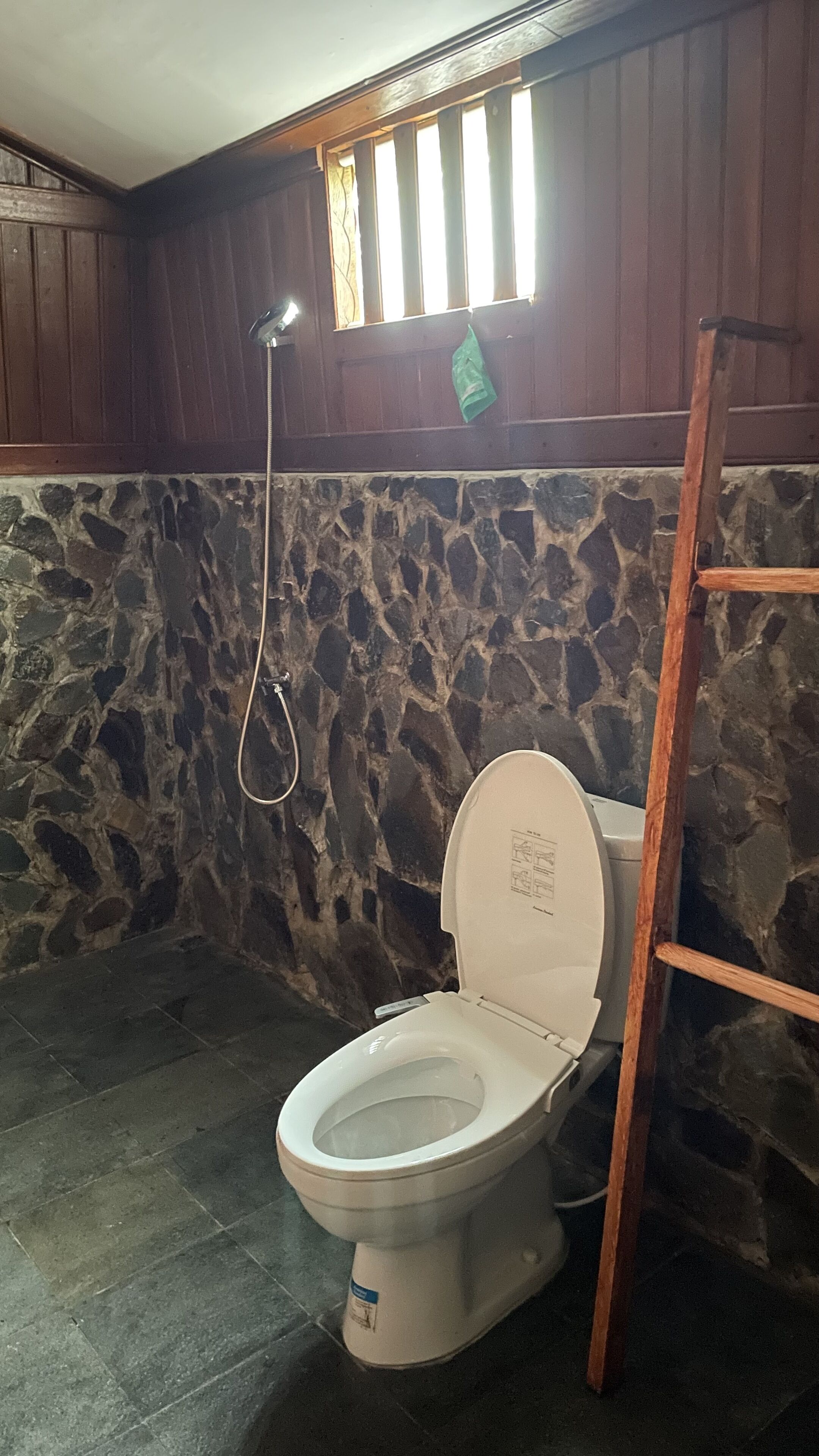 A bathroom with a stone wall, a wooden ceiling, and a white toilet.