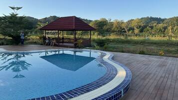 A swimming pool with a tiled edge, a wooden deck, and a gazebo in a natural setting.