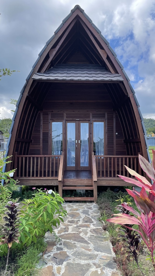 A wooden cabin with a steep gable roof, a stone pathway leading to the entrance, and a wooden porch with a railing.