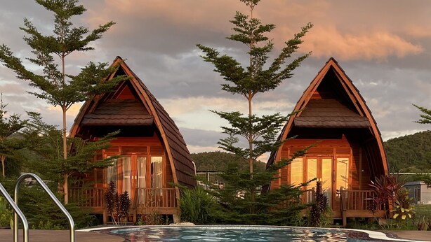 A swimming pool with wooden cabins in the background. - Raffles Inn Labuan Bajo (Labuan Bajo)