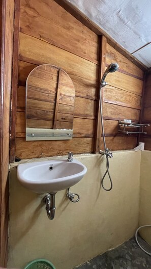 A bathroom with a wooden wall, a white sink, a mirror, and a shower.