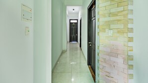 A hallway with a tiled floor, a wall-mounted light switch, and a door with a brick-patterned wall. - Loan Anh 2 Hotel (Da Nang)