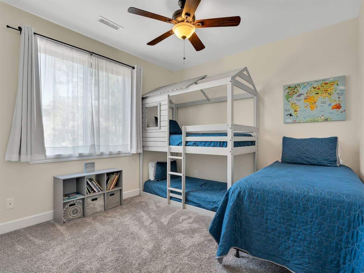A bedroom with bunk beds, a ceiling fan, a world map on the wall, and a bookshelf.