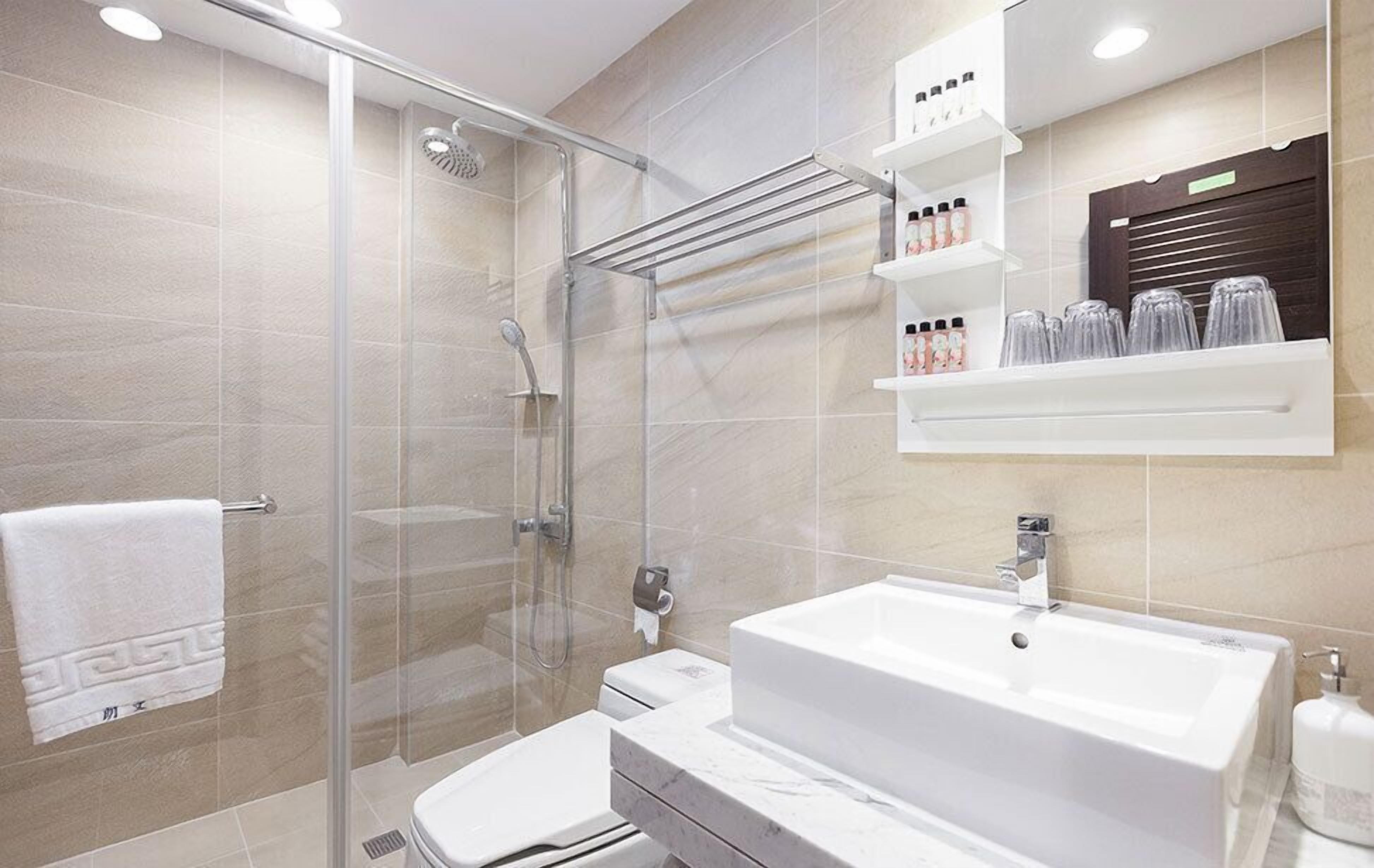 A modern bathroom with a glass shower enclosure, a white sink, and a towel rack.
