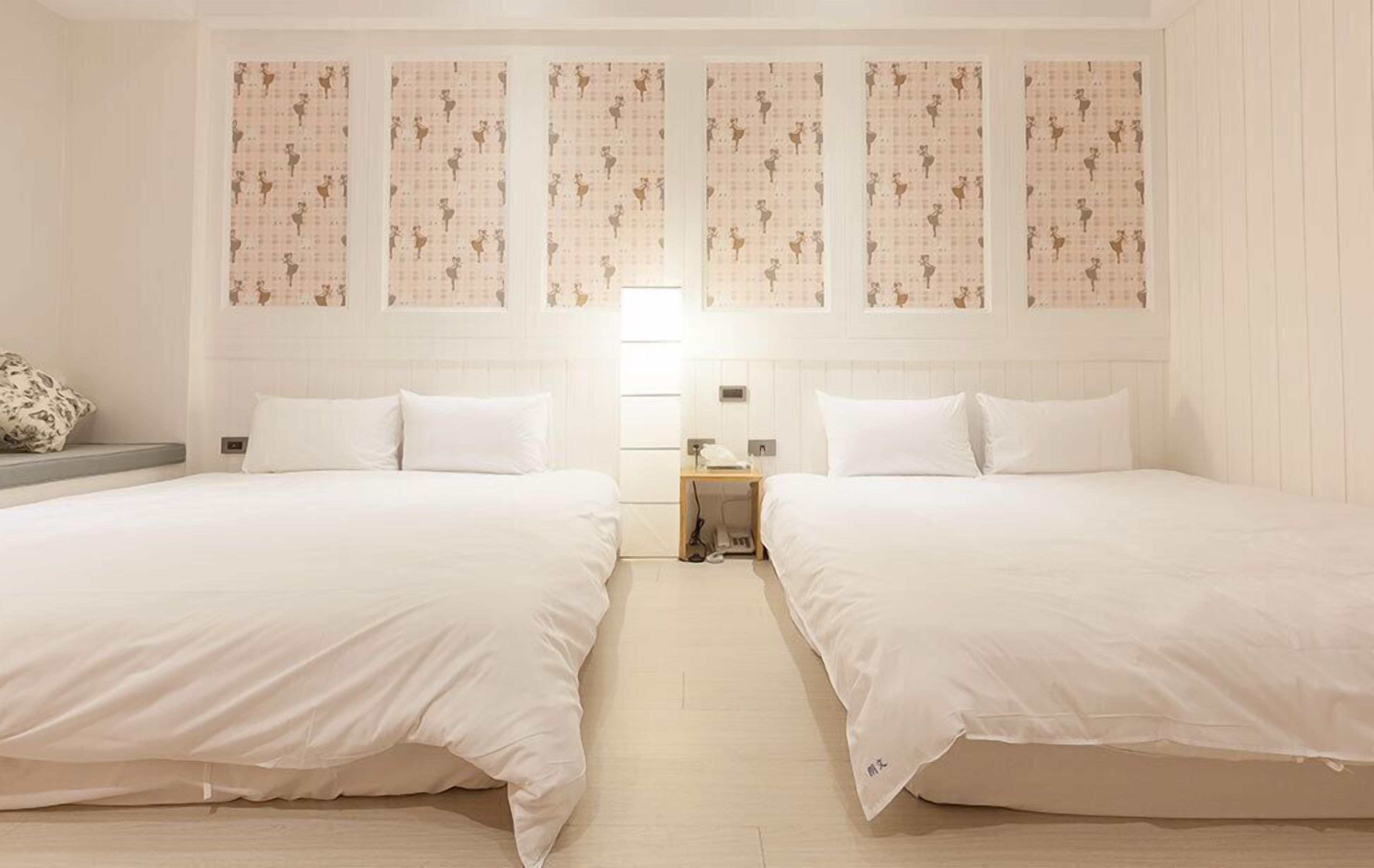 Habitación de hotel con dos camas, una mesita de noche pequeña y una pared con papel tapiz estampado.