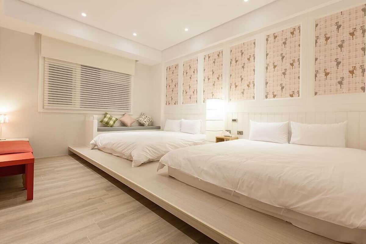 A bedroom with two beds, a bench, and a window with blinds.
