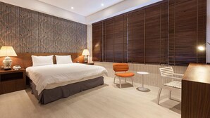 A modern hotel room with a large bed, two bedside tables with lamps, a small round table, a chair, and a large window with blinds. - Lanven Art House (Hualien City)
